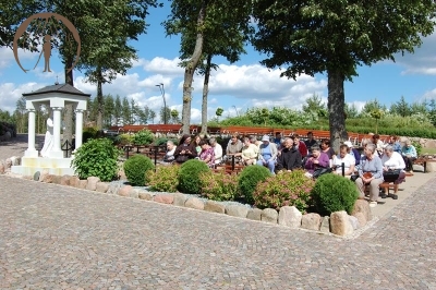Pielgrzymi siedzą na ławeczkach przy Sanktuarium Matki Bożej Bolesnej, chwila przed modlitwą