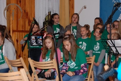 Świetlica Domu Nadziei, koncert Nutek Chwały ubranych w zielone koszulki z nazwą i logiem zespołu,w pierwszym planie siedzą dwie dziewczynki i grają na cymbałkach, w drugim planie stoją dziewczęta i śpiewają obok z lewej strony dziewczynka gra na skrzypcach