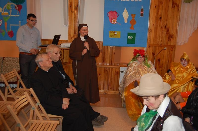 Świetlica Domu Nadziei, Matka Radosława mówi przez mikrofon, obok siedzą księża, aktorzy