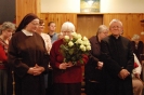Hol przed Kaplicą w Domu Nadziei, pani Halina trzyma białe róże w towarzystwie ks. Antoniego i siostry Szymony