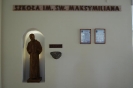 Ośrodek w Laskach, hol w szkole im. Św. Maksymiliana, podświetlona figura Św. Maksymiliana we wnęce w ścianie, po prawej stronie wmurowany w ścianę kamień z relikwiami pierwszego stopnia Patrona szkoły, u góry na ścianie napis: Szkoła im. Św. Maksymiliana